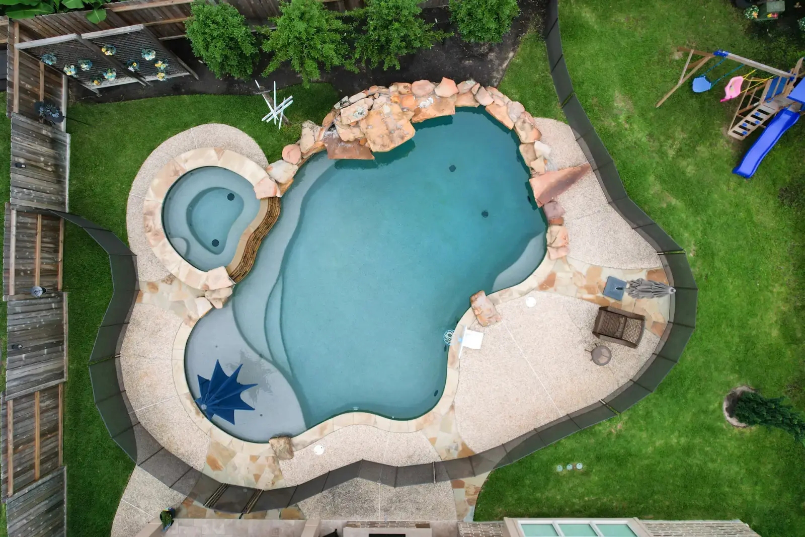 Drone view of a freeform pool with an attached spa, star mosaic steps and a boulder waterfall