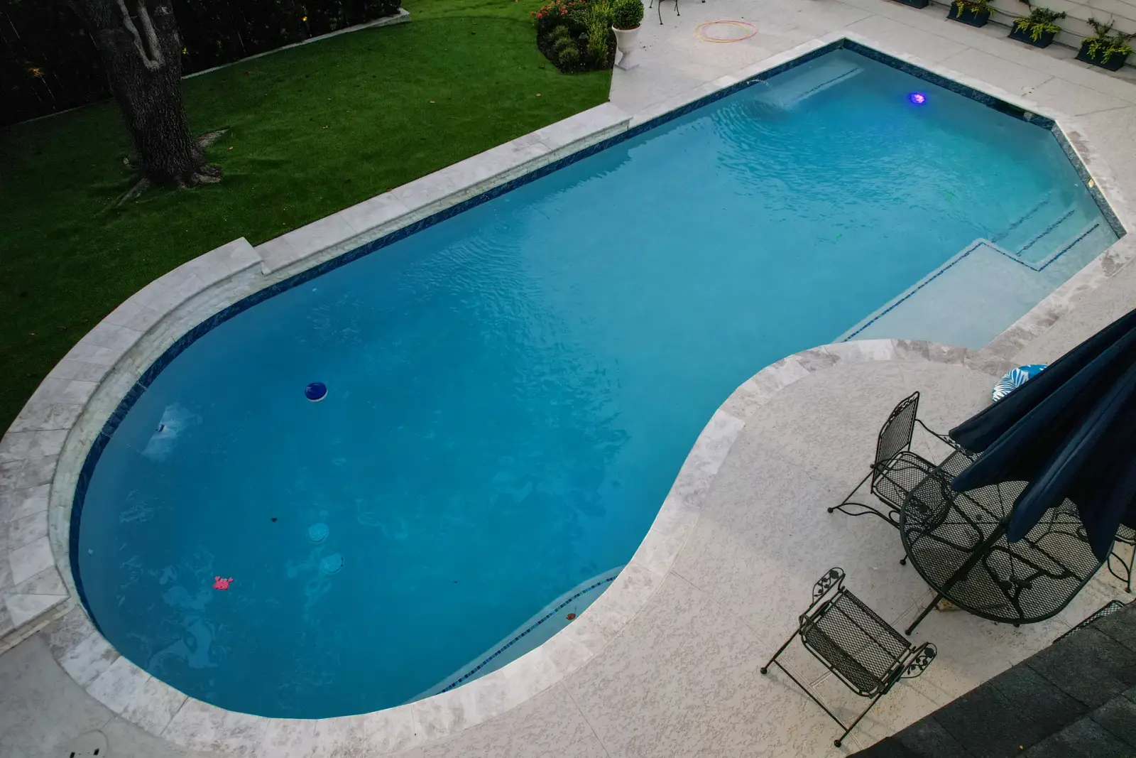 Drone view of a geometric pool with a travertine deck beside a lawn