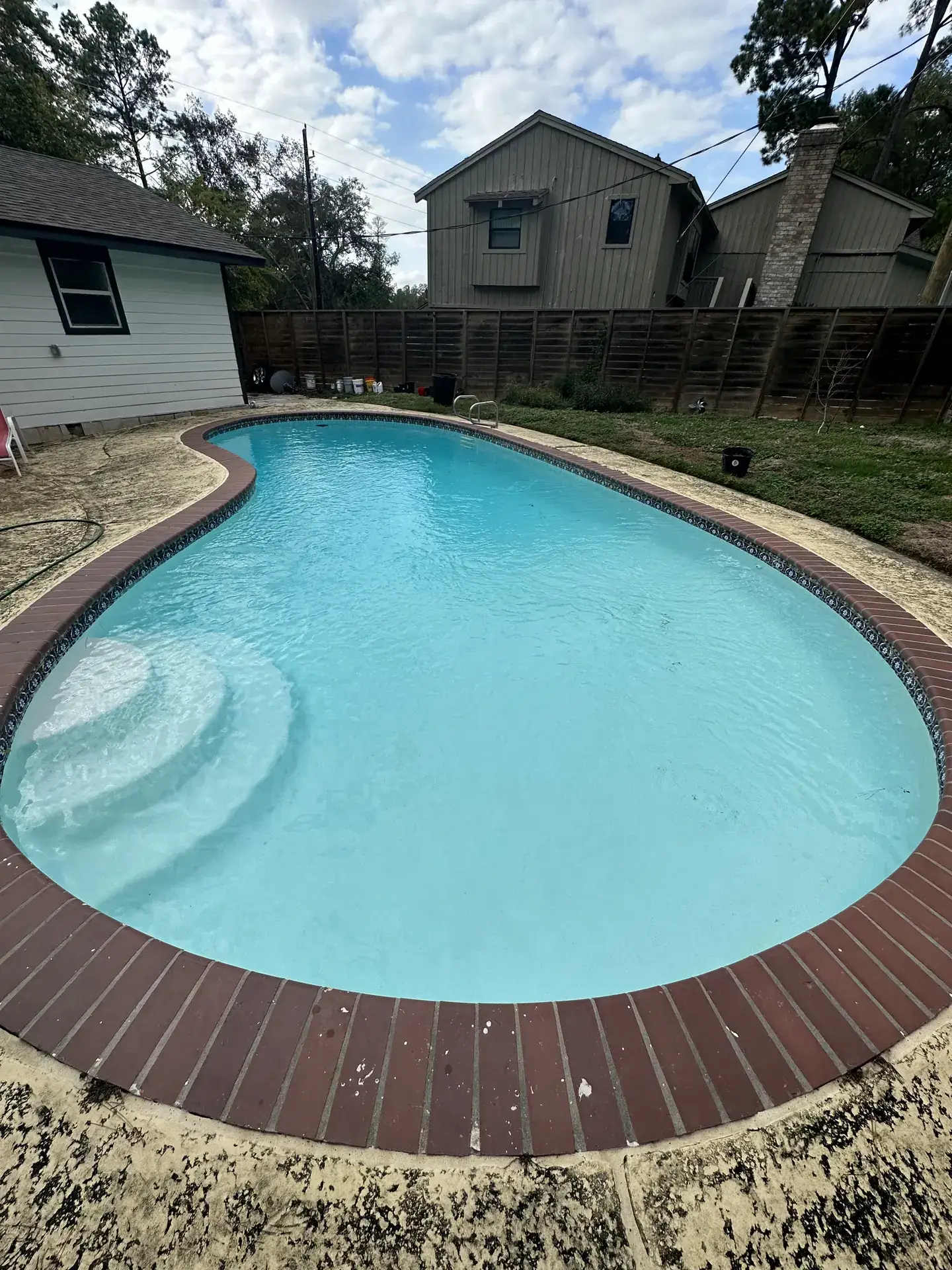 Kidney pool refilled with clear blue water over new white plaster, with red brick coping
