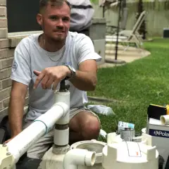 Aloha technician kneeling beside pool pump and filter plumbing during an equipment repair