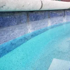 Close view of blue waterline tile under light stone coping at the edge of a pool