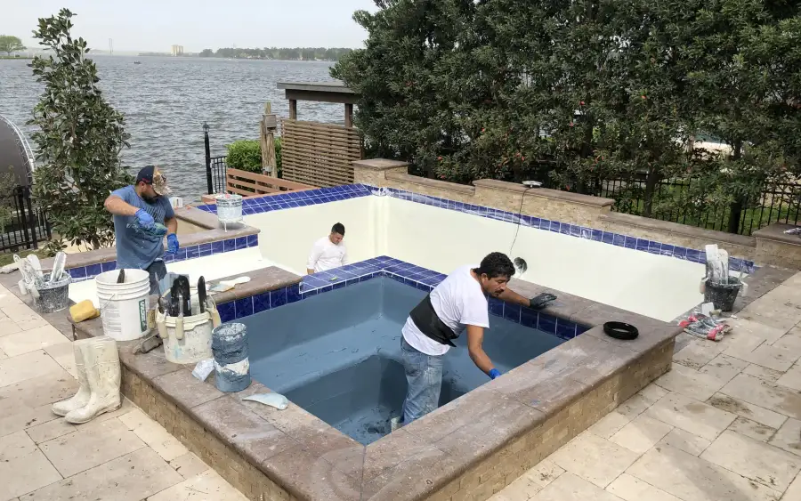 Aloha crew replastering a raised square spa with blue waterline tile beside a lake